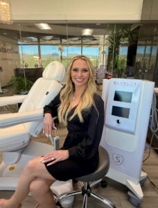 Cara Greer, CMLT, seated beside the Scarlet SRF radiofrequency microneedling device at Rejuvenate Renew med spa in Scottsdale, Arizona